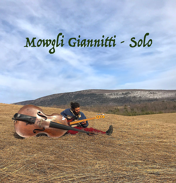 Mowgli Giannitti with cello and guitar sitting in a field