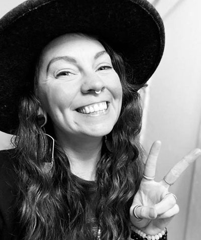 Musician Sarah Bell wearing her signature hat with her fingers showing a peace sign