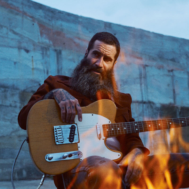 JP Harris sitting behind flames with his guitar